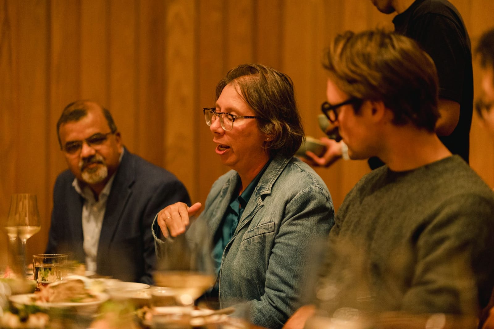 A guest in a denim jacket speaks across the dinner table while two other engineering leaders listen